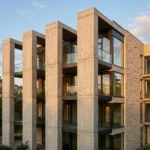 Façade d'immeuble résidentiel moderne avec trois piliers structurels apparents en pierre claire, photographiée en contre-plongée sous lumière naturelle dorée